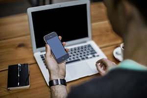 A person Looking at a smartphone while using a laptop
